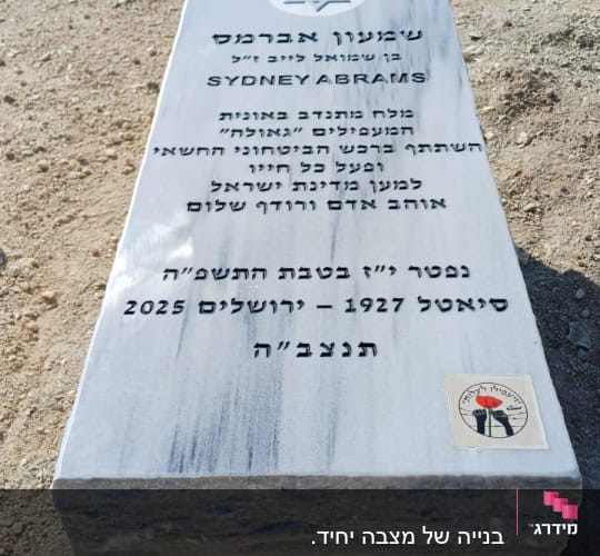 מצבה עם כיתוב בעברית ואנגלית על רקע אדמה